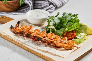 Grilled shrimps with sauce on concrete background. Aesthetic composition with prawn skewer and fresh herbs. Shrimps on grill in summer menu. Seafood skewer in minimal style.