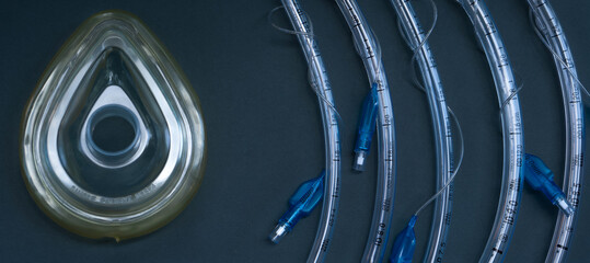 Endotracheal tubes of different diameters and a mask for a ventilator lie on a dark background.  close-up.  medical instruments, anesthesia instruments - obrazy, fototapety, plakaty