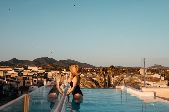 Anonymous feminine lady relaxing in pool in rooftop at sunset