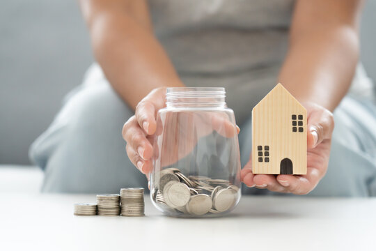 Woman Save Money Coin In Jar For New Property Living Investment, Wooden House And Jar Coins Savings Concept.