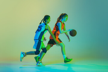 Streetball. Female basketball players, young girls, teen in action with basketball ball isolated on neoned background. Concept of sport, team, enegry, competition, skills