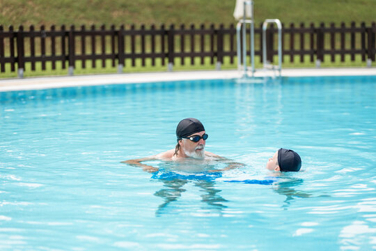 Cheerful kid swimming in pool with bearded grandfather on sunny day
