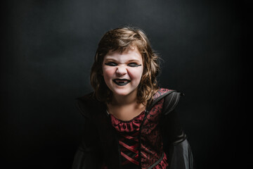 Cheerful little kid with black lips and vampire costume during carnival