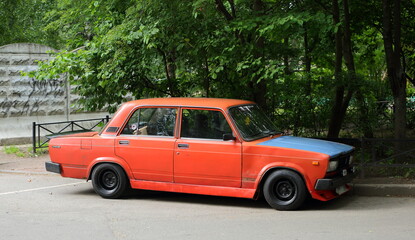 An old red Soviet car with a blue hood is parked next to the lawn, Podvoysky Street, St. Petersburg, Russia, July 2022