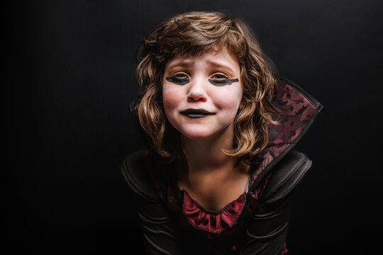 Sad little child in Halloween costume crying in dark studio