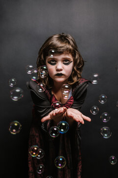 Serious little kid with black lips catching soap bubbles during carnival