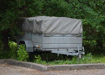 Two-wheeled gray awning trailer for a passenger car stands on a green lawn