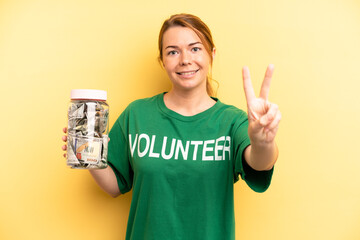 pretty blonde young woman smiling and looking friendly, showing number two. donation and volunteer...