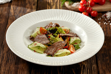 Steak salad with zucchini, tomatoes and lettuce on white plate. Fresh salad with roast beef and vegetables on wooden table in rustic style. Meat and vegetables salad on dark wooden background.