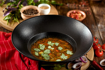 Georgian food - kharcho soup with coriander leaf in black plate on wooden table. Traditional georgian soup with lamb meat and spices in rustic style. Caucasian cuisine on dark wooden background.