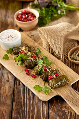 Traditional georgian food - meat dolma on plate with sauce in rustic style. Caucasian dish - stuffed grape leaves with minced meat and pomegranate on wooden background. Composition with meat dolma.