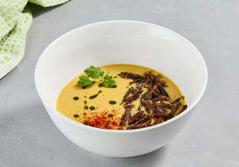 Cream soup with vegetables and crispy meat. Pea cream soup with spices on concrete background. Aesthetic composition with vegetables soup in white ceramic bowl