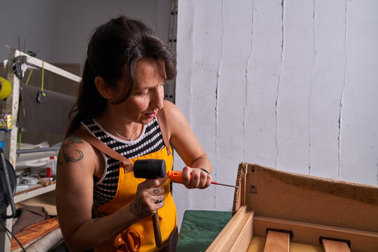 Professional female carpenter fixing wooden plank with screwdriver and hammer