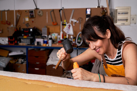 Professional female carpenter fixing wooden plank with screwdriver and hammer