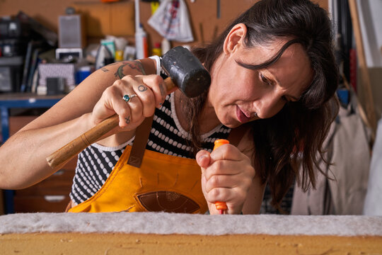 Professional female carpenter fixing wooden plank with screwdriver and hammer