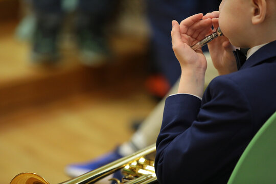 A Little Musician Sitting On A Chair Musical Instrument Trumpet On His Knees Holds A Mouthpiece In The Palm Of His Hand Blowing Swollen Cheeks Image Close-up