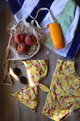 Striped towel, yellow floral swimming suit, sunglasses, mesh tote with fresh peaches, seashell and sunscreen. Beach essentials, flat lay.