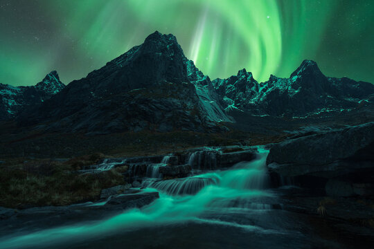 Fast waterfall flowing through rocks under bright Northern Lights