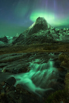 Fast waterfall flowing through rocks under bright Northern Lights