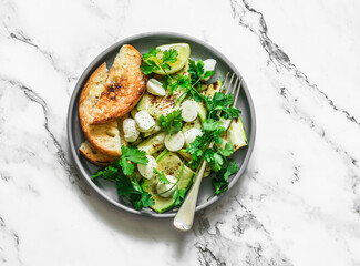 Grilled zucchini, mozzarella, cilantro salad with olive oil, lemon, garlic, pepper sauce on a light background, top view