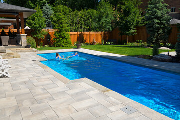 Mother and daughter swimming in new back yard pool with  patio of pavers and green lawn and gardens - obrazy, fototapety, plakaty
