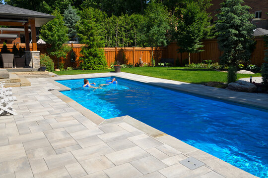 Mother and daughter swimming in new back yard pool with  patio of pavers and green lawn and gardens