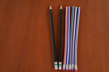 5 unsharpened wooden pencils (with multi-colored stripes) and sharpened pencil 2 black are placed...