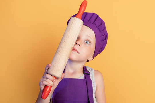 Cute little child holding rolling pin near face and looking at camera