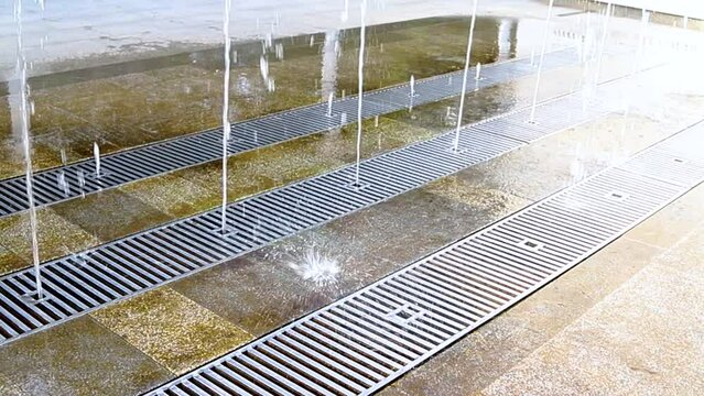 Fountain in the city park. A jet of water escapes from under the grate to the ground. Children's entertainment in the park. Cool water on a hot day.