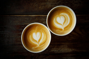 Two cups of cappuccino with a heart latte art. Vintage wooden background, top view.