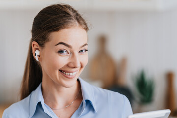 Close up portrait of cute blonde caucasian girl with ponytail l smiling using earphones, listening...