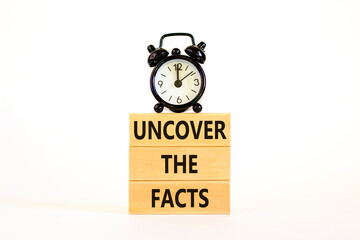 Uncover the facts symbol. Concept words Uncover the facts on wooden blocks on a beautiful white table white background. Black alarm clock. Business and uncover the facts concept. Copy space.