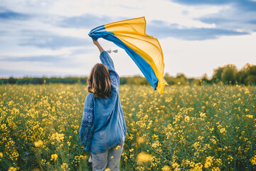 Ukrainian patriot woman waving national flag in canola yellow field. Rare, back view. Ukraine...