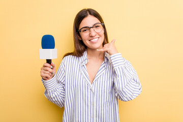 Young caucasian presenter TV woman isolated on yellow background showing a mobile phone call gesture with fingers.