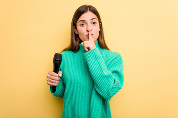 Young caucasian singer woman isolated on yellow background keeping a secret or asking for silence.