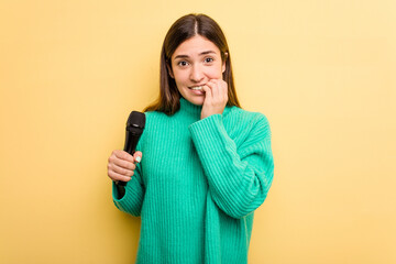Young caucasian singer woman isolated on yellow background biting fingernails, nervous and very...