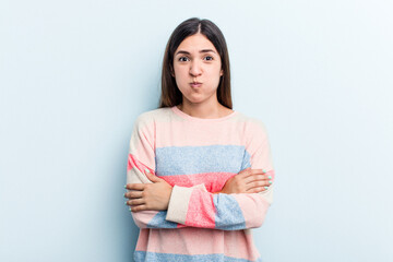 Obraz premium Young caucasian woman isolated on blue background blows cheeks, has tired expression. Facial expression concept.