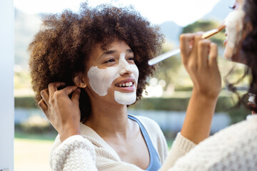 Smiling biracial female friends applying beauty cream on each others faces in balcony
