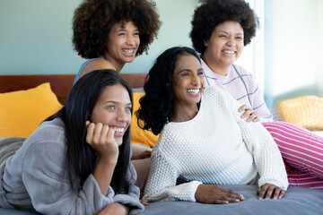 Cheerful biracial young female friends looking away while spending leisure time together on bed