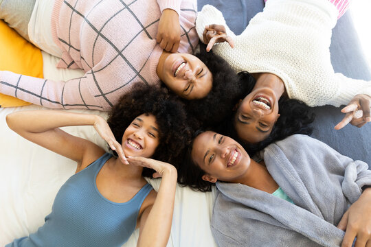 High angle portrait of happy biracial young female friends gesturing and lying while relaxing on bed