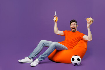 Full body young fan man he in orange t-shirt cheer up support football sport team hold soccer ball...