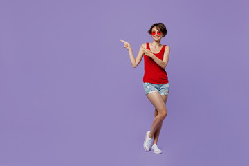 Fototapeta na wymiar Full body young smiling fun woman 20s she wear red tank shirt eyeglasses pointing index finger aside indicate on workspace area copy space mock up isolated on plain purple backround studio portrait