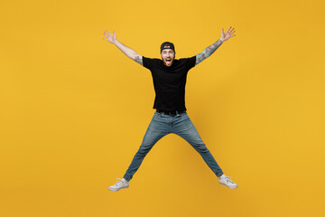 Fototapeta na wymiar Full body young overjoyed excited exultant happy jubilant bearded tattooed man 20s he wears casual black t-shirt cap jump high with outstretched hands legs isolated on plain yellow wall background