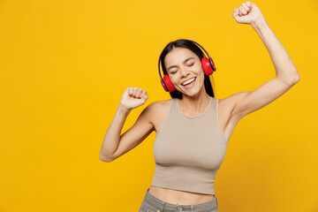 Young joyful happy latin woman 30s she wear basic beige tank shirt headphones dance listen to music...