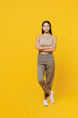 Full body serious calm attractive young latin woman 30s she wearing beige tank shirt look camera hold hands crossed folded isolated on plain yellow backround studio portrait People lifestyle concept