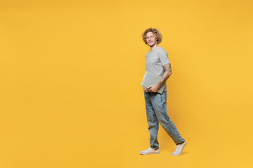Fototapeta na wymiar Full body young student smiling cheerful fun caucasian man 20s he wear grey t-shirt look camera hold use closed laptop pc computer isolated on plain yellow backround studio. People lifestyle concept.