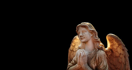An ancient statue of guardian angel against black background.  Copy space.