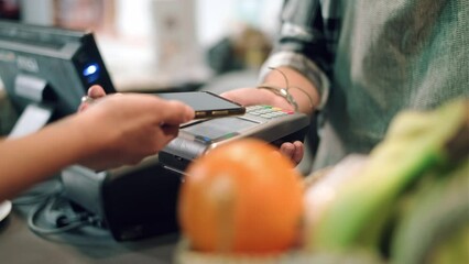 Video of close up of woman paying for the purchase with her smartphone via NFC in a grocery store. - Powered by Adobe