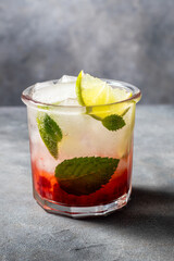 cold detox water with lime, strawberry, mint in the glass with ice cubes on gray background. close up