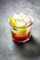 cold detox water with lime, strawberry, mint in the glass with ice cubes on gray background. close up